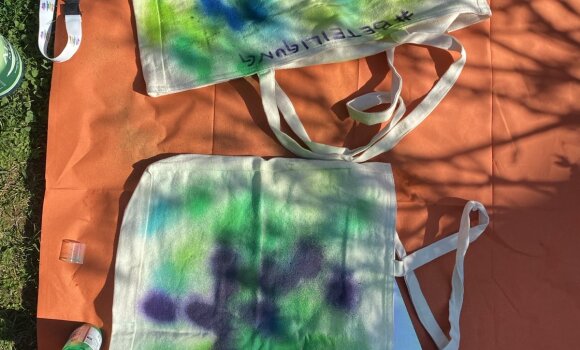 Zu sehen sind zwei Stofftaschen, die mit Sprühfarben bunt gestaltet wurden. 