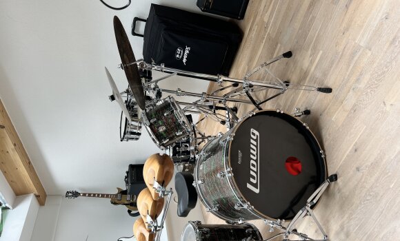 Zu sehen ist ein Musikraum, mit vielen verschiednenen Instrumenten. Zum Beispiel einem Schlagzeug, Gitarren und Lautsprechern. 